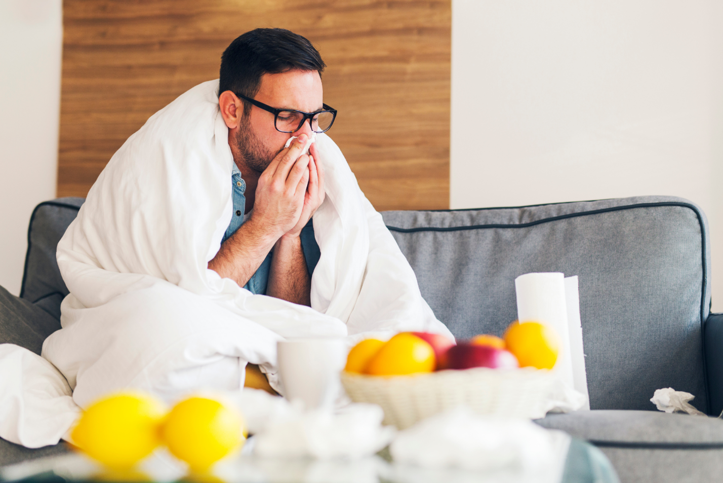 man sick and blowing his nose on the couch